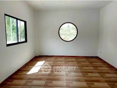 Spacious empty room with unique circular window and wooden flooring