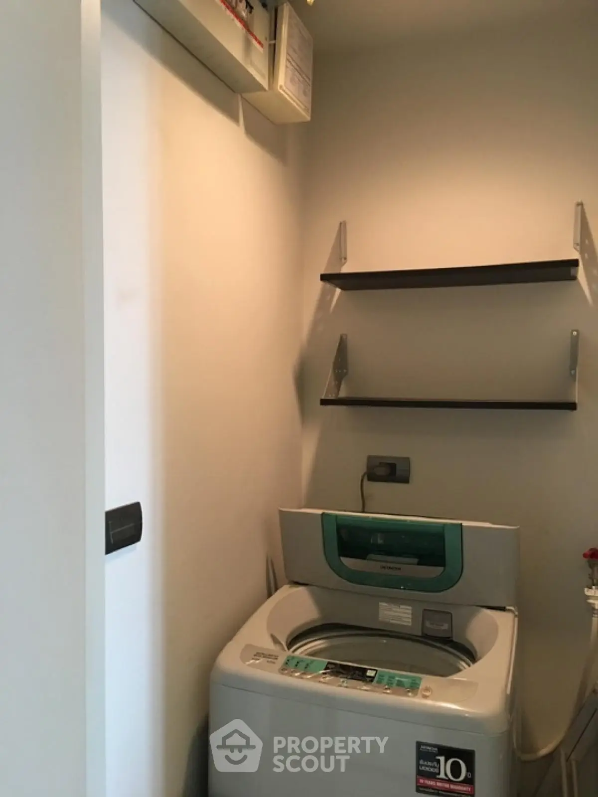 Compact laundry area with modern washing machine and wall shelves in a cozy apartment.