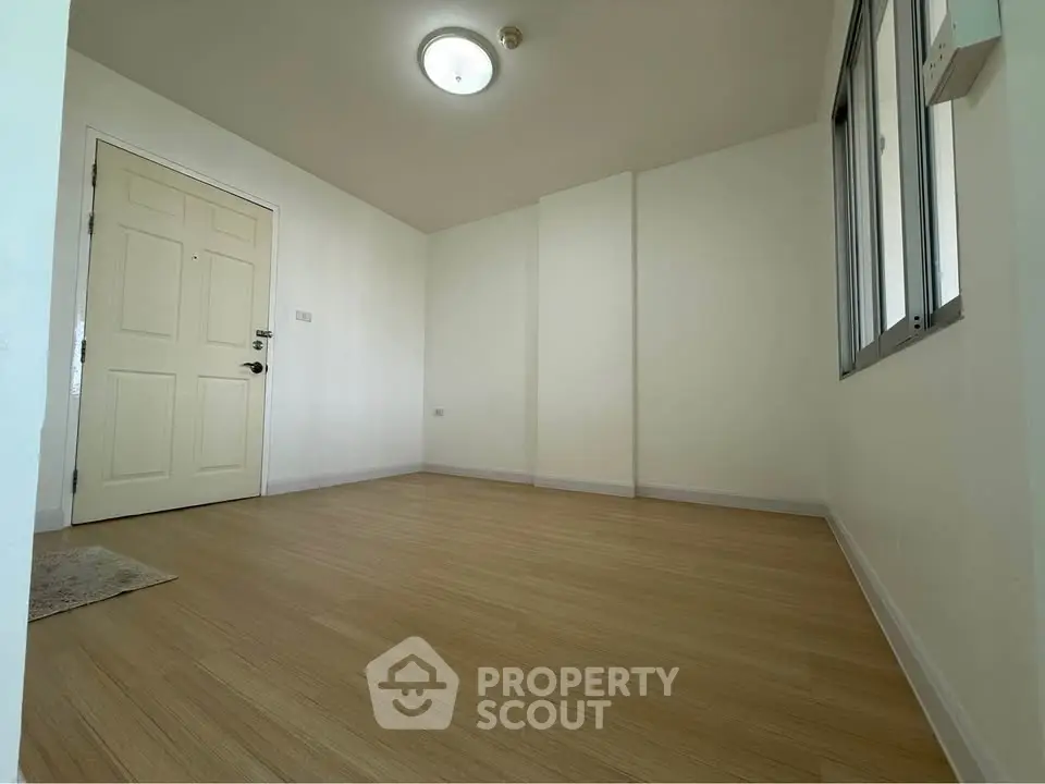 Spacious empty room with wooden flooring and large window, perfect for customization.