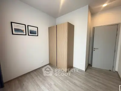 Minimalist bedroom with wooden wardrobe and framed art on white walls.