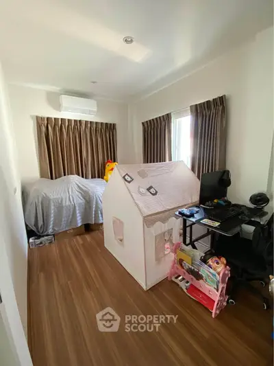 Charming bedroom with wooden flooring, children's playhouse, and cozy workspace, perfect for family living.