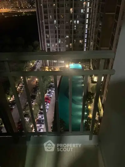 Stunning night view from a high-rise balcony overlooking a pool and cityscape.