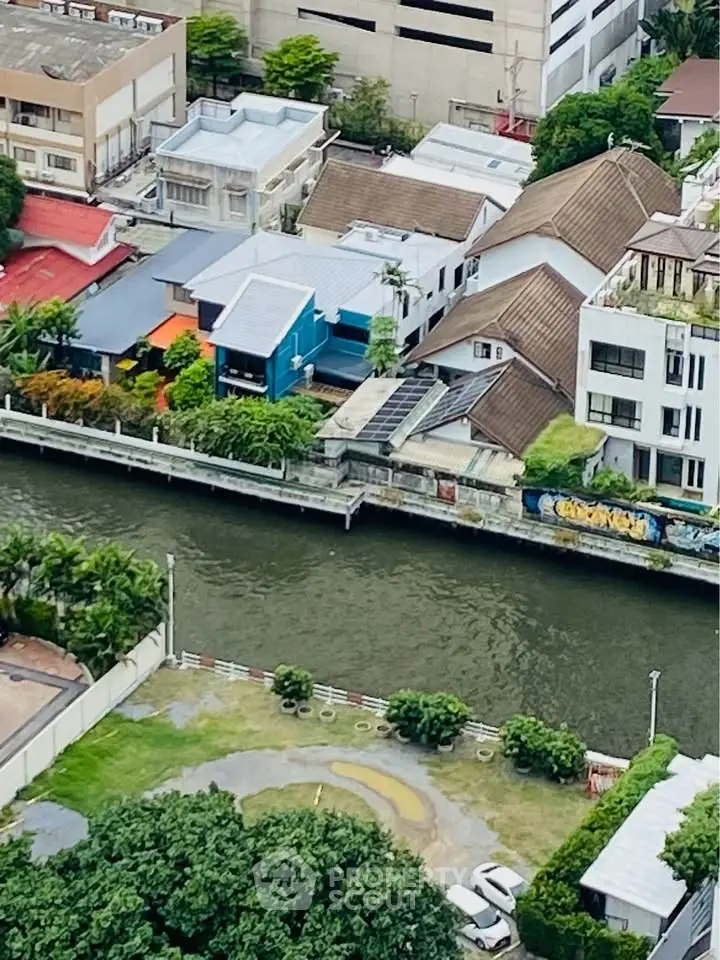 Aerial view of riverside residential area with modern houses and lush greenery.