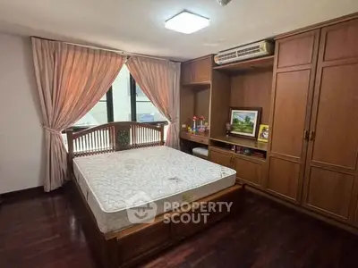 Spacious bedroom with wooden furniture and large window for natural light.