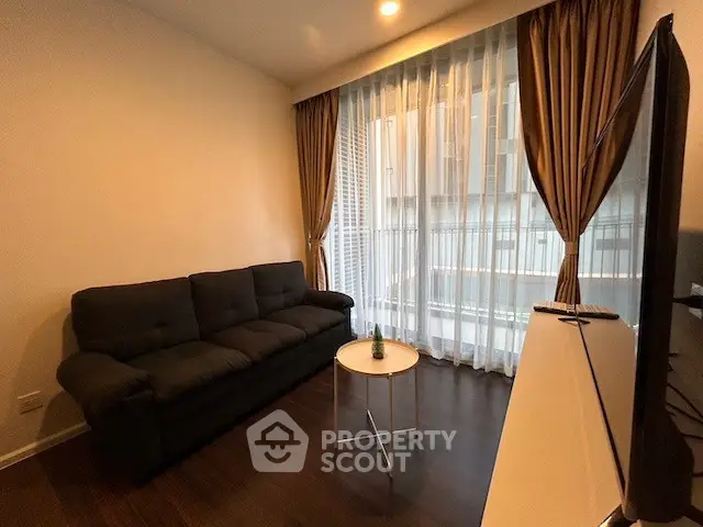Cozy living room with dark sofa and large window with sheer curtains, perfect for relaxation.