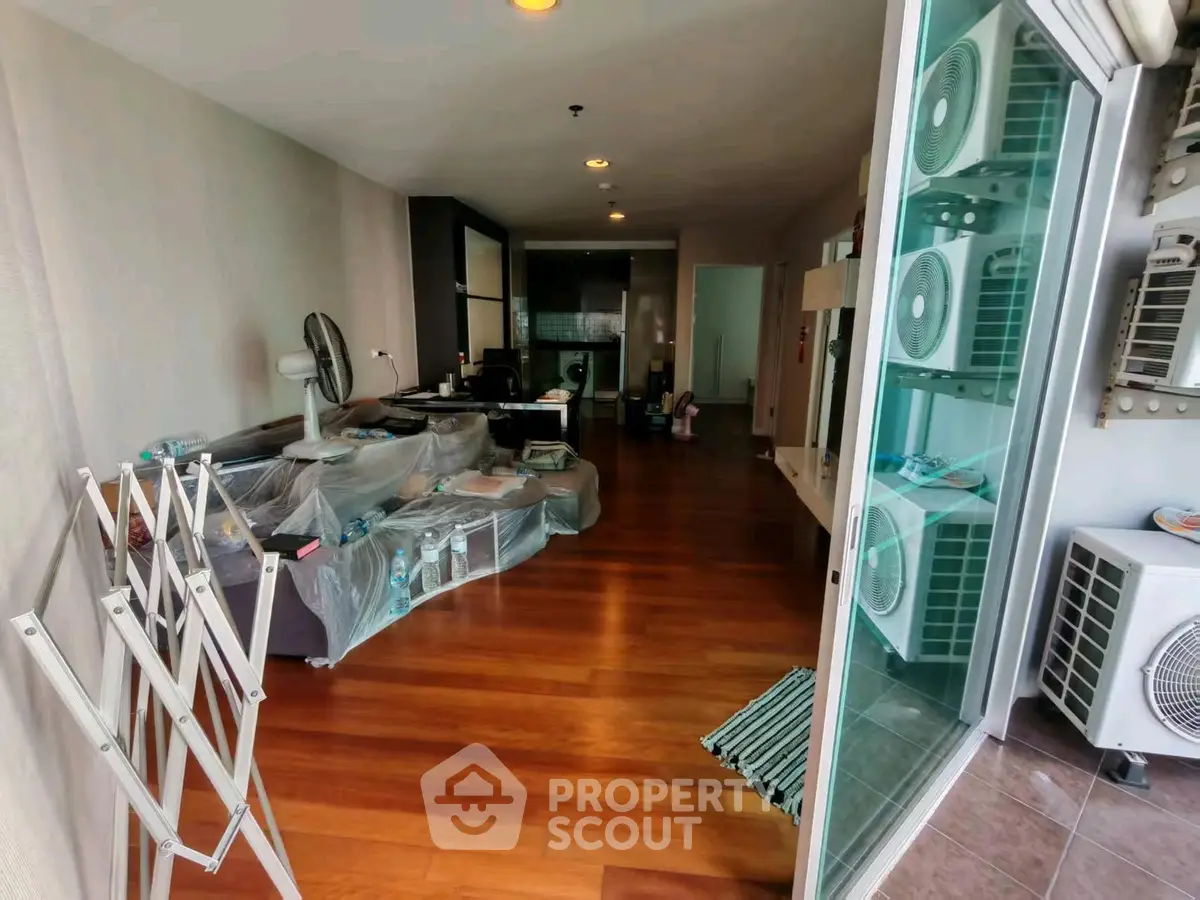 Spacious living room with wooden flooring and modern decor, featuring large windows and air conditioning units.