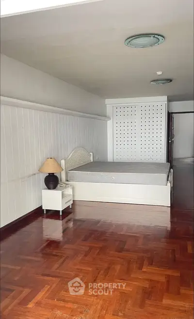Spacious bedroom with wooden flooring and built-in closet, featuring a cozy bed and stylish lamp.