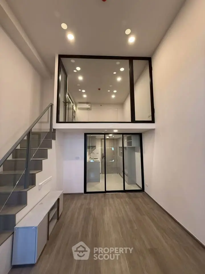 Modern loft apartment with high ceilings and sleek staircase, featuring a mezzanine level and stylish lighting.