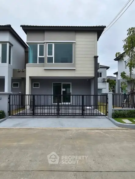 Modern two-story house with sleek design and gated driveway in a suburban neighborhood.