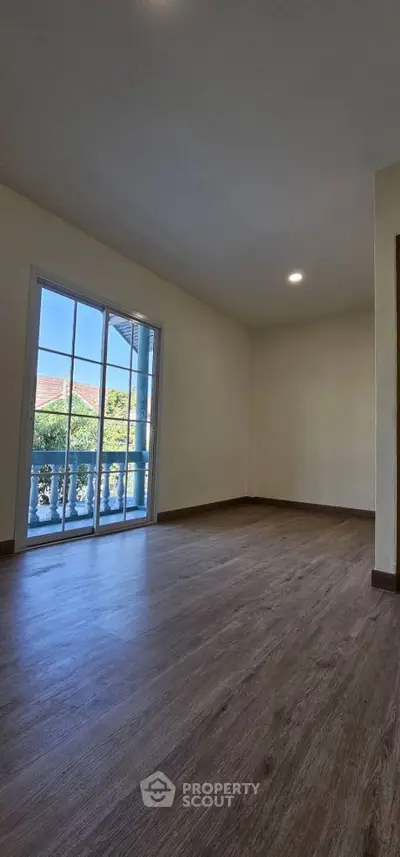 Spacious empty room with wooden flooring and large window overlooking greenery.