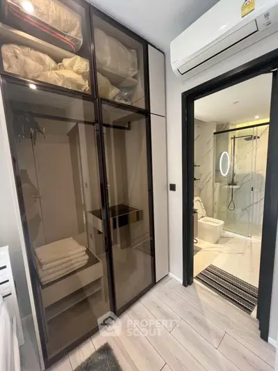 Modern bedroom with glass wardrobe and ensuite bathroom featuring sleek design.