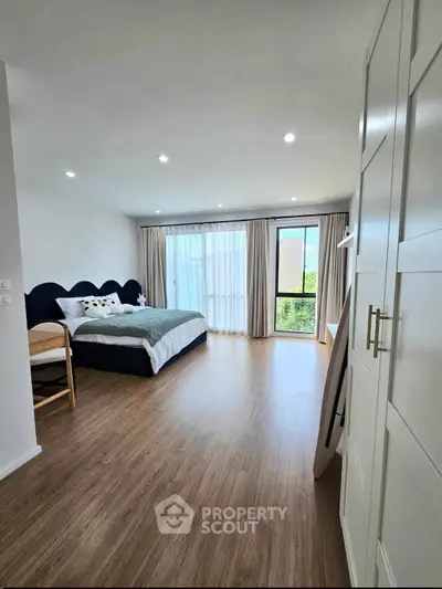 Spacious bedroom with modern decor and large window offering natural light and serene views.
