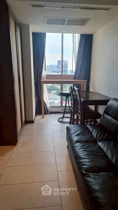 Cozy living room with city view, featuring a sleek black leather sofa and dining area by the window.