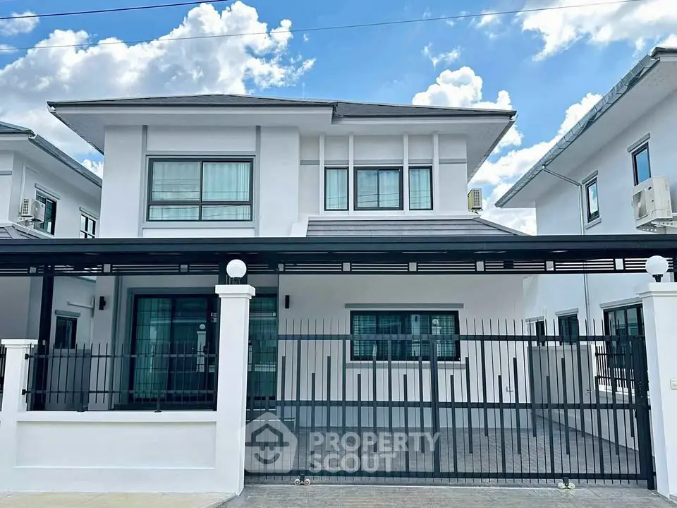 Modern two-story house with sleek design and gated entrance under a clear blue sky.