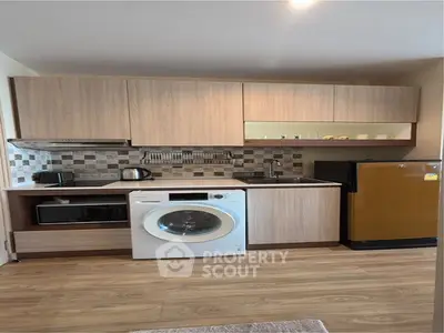Modern kitchen with wooden cabinets, washing machine, and compact fridge in cozy apartment.