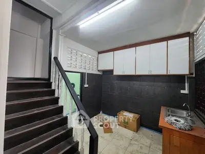 Compact kitchen with dark tiles and wooden cabinets, featuring a staircase and natural light.