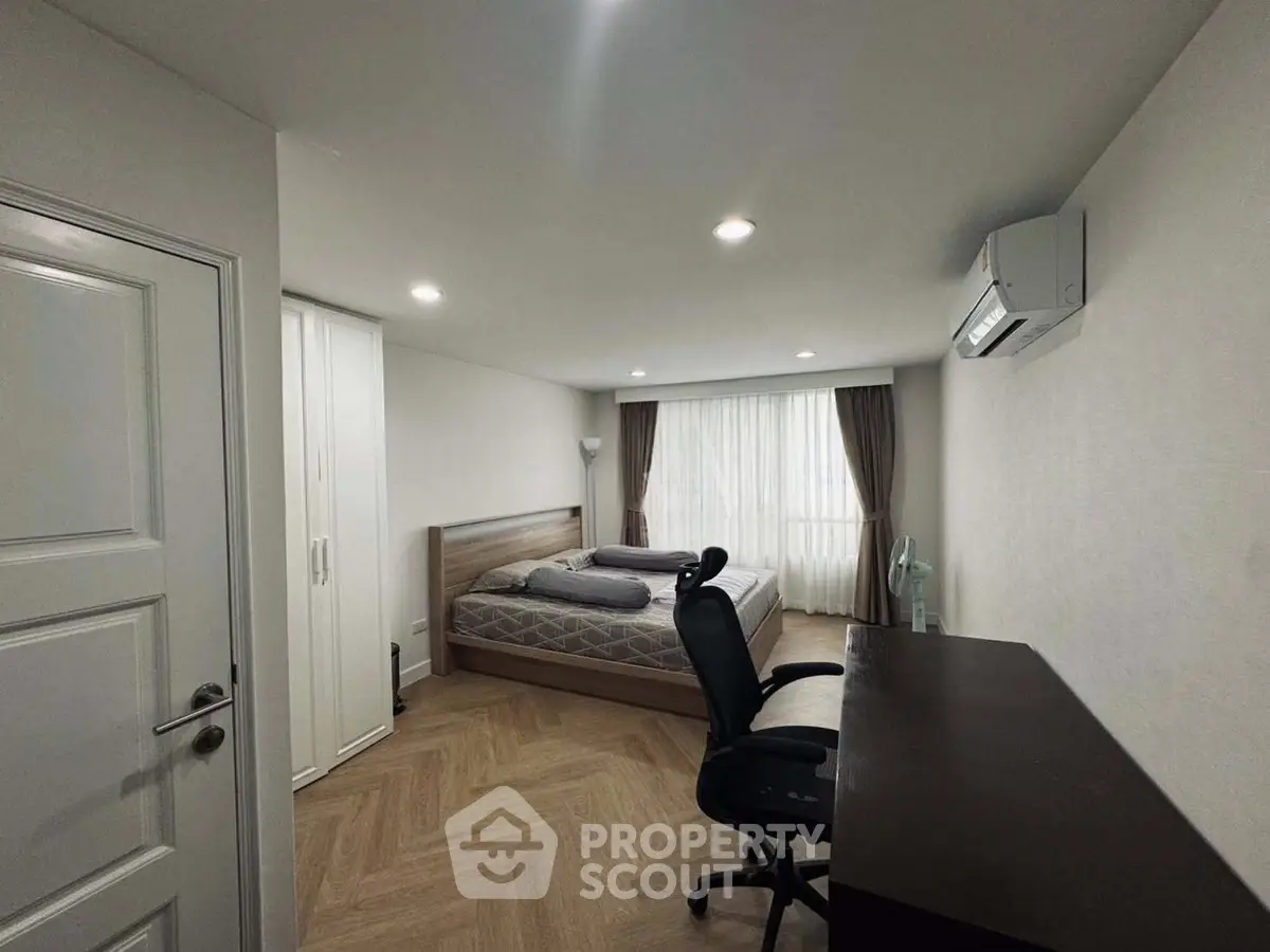 Modern bedroom with wooden flooring, large window, and sleek furniture in a stylish apartment.
