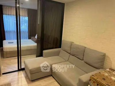 Modern living room with cozy gray sofa and glass partition leading to bedroom.