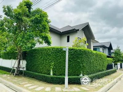 Modern two-story house with lush green hedges and a well-maintained garden.