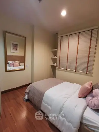 Cozy bedroom with wooden flooring and stylish decor, featuring a comfortable bed and elegant mirror.