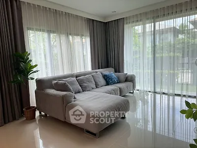 Spacious living room with modern gray sectional sofa and large windows offering lush garden views.