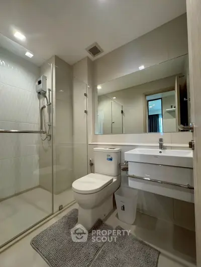 Modern bathroom with glass shower, sleek fixtures, and large mirror in a contemporary apartment.