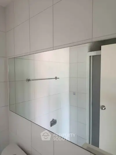 Modern bathroom with sleek white tiles and a large mirror reflecting a shower area.