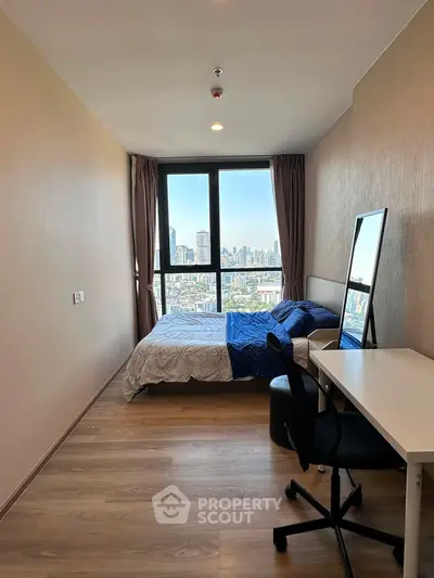 Modern bedroom with city view, featuring a cozy bed, desk, and large window for natural light.