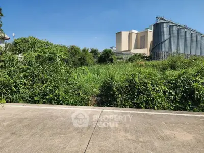 Vacant land with lush greenery and industrial backdrop, ideal for development opportunities.