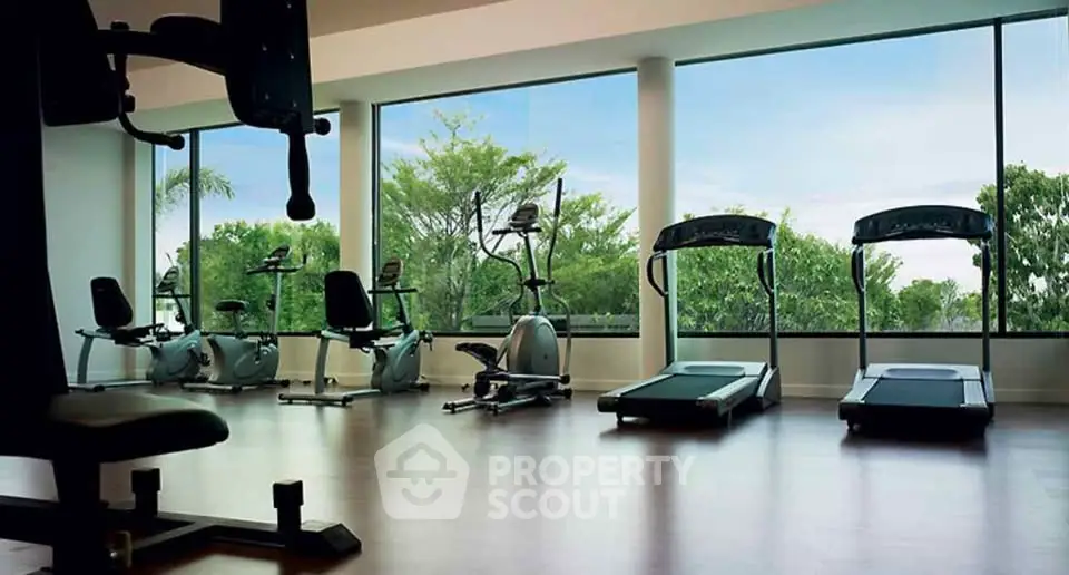 Spacious gym with modern equipment and scenic garden view through large windows.
