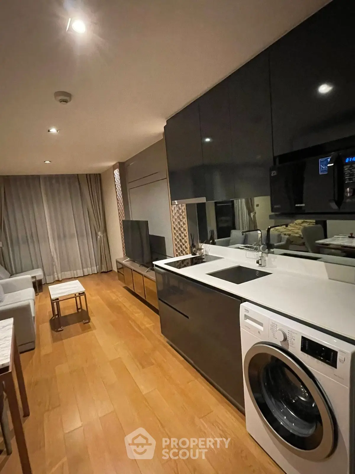 Modern living room with sleek kitchen and washing machine, featuring wooden flooring and stylish decor.