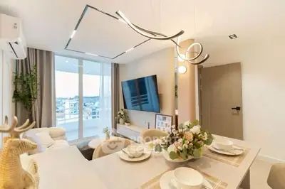 Modern living room with elegant dining area and large TV, featuring stylish lighting and panoramic window view.
