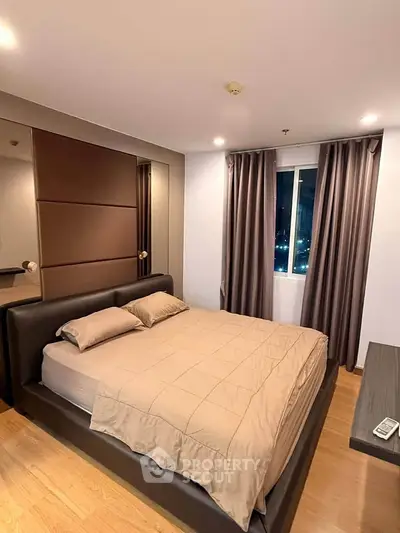 Modern bedroom with cozy lighting and city view, featuring a stylish bed and elegant curtains.