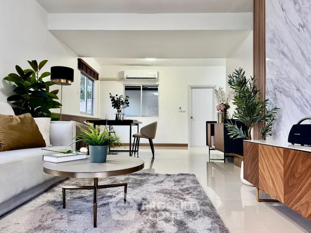 Spacious modern living room with elegant decor and natural light, featuring stylish furniture and lush greenery.