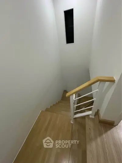 Modern staircase with wooden steps and sleek railing in a minimalist home interior.
