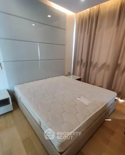 Spacious bedroom with modern design and natural light, featuring a comfortable mattress and elegant curtains.