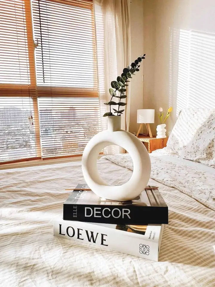 Stylish bedroom with modern decor and natural light, featuring a unique vase and designer books.
