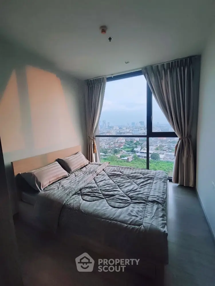 Modern bedroom with large window offering stunning city views and elegant decor.