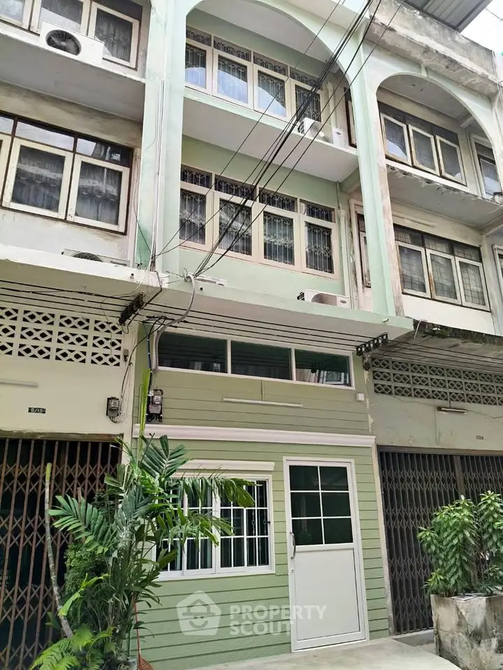 Charming multi-story building with green facade and lush plants in urban setting.