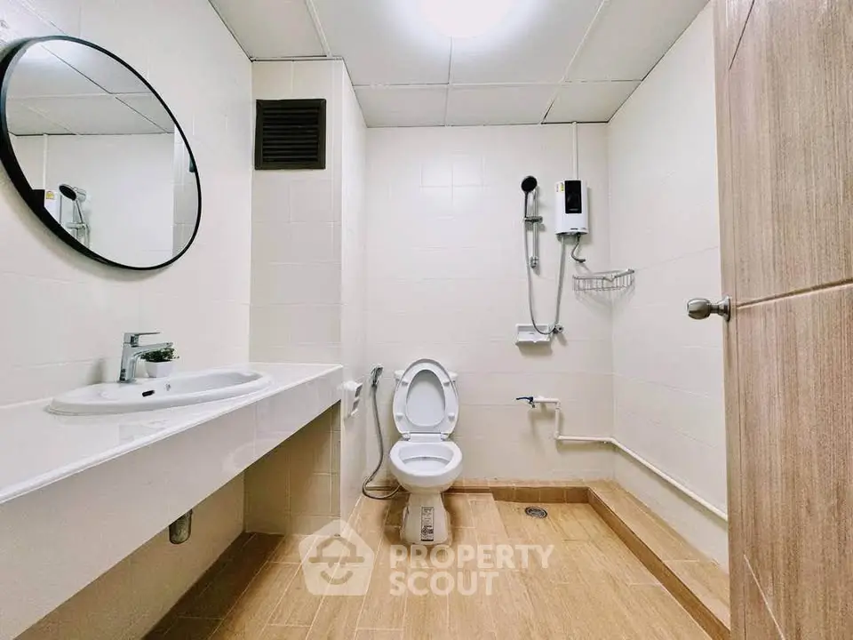 Modern bathroom with sleek fixtures and wooden flooring, featuring a round mirror and shower area.