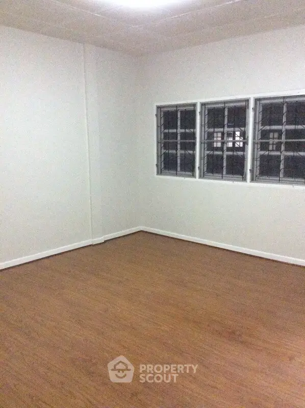 Spacious empty room with wooden flooring and barred windows, ideal for customization.