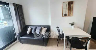 Modern living room with sleek black sofa and dining area, featuring a large window for natural light.