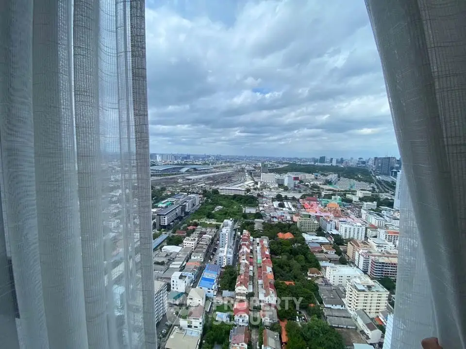 Stunning cityscape view from high-rise apartment window with sheer curtains framing the skyline.