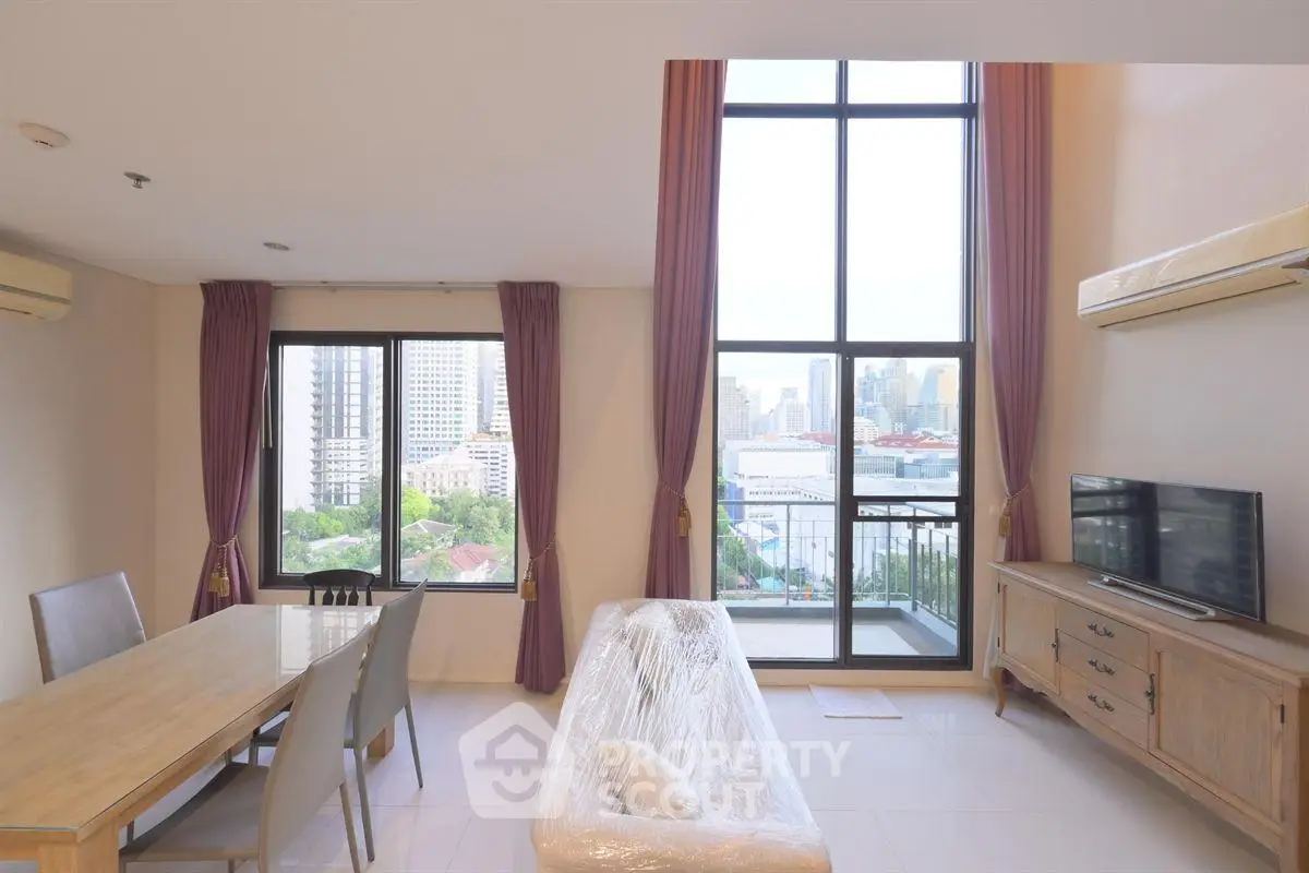 Spacious living room with high ceilings and city view, featuring modern furniture and large windows.