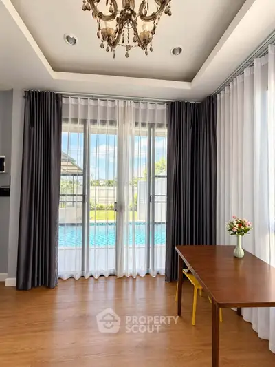 Elegant living room with pool view, featuring chandelier and wooden table, perfect for modern living.