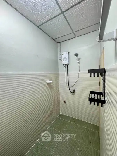 Compact bathroom with green tiled floor and wall-mounted shower unit.