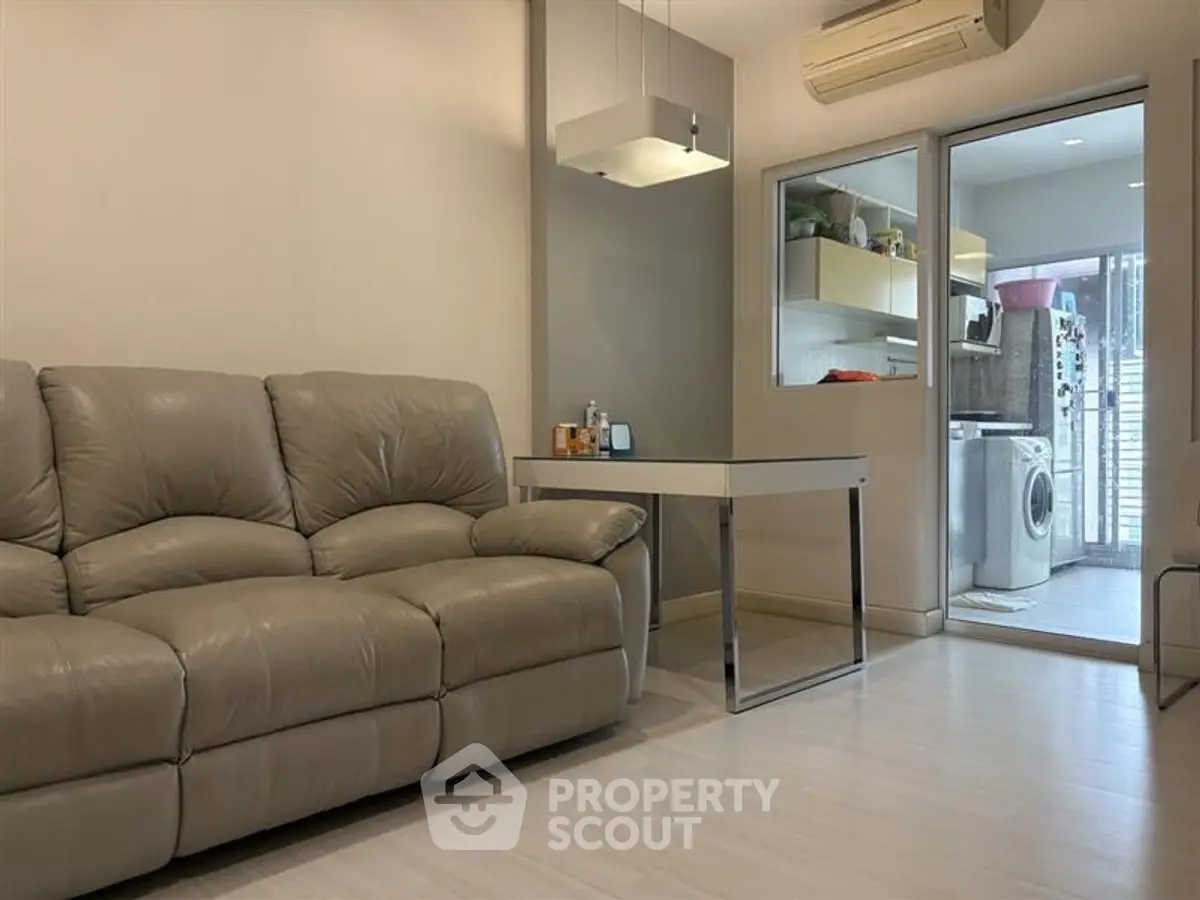 Modern living room with leather sofa and adjacent laundry area featuring washing machine.