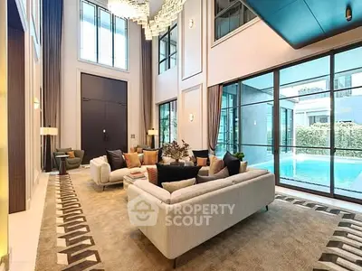 Luxurious living room with high ceilings and pool view, featuring elegant decor and large windows.