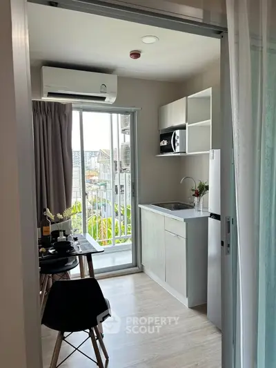 Modern compact kitchen with dining area and balcony view in urban apartment