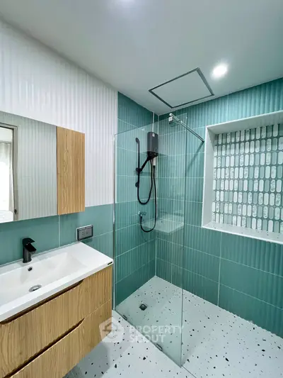 Modern bathroom with teal tiles, glass shower, and sleek wooden vanity.